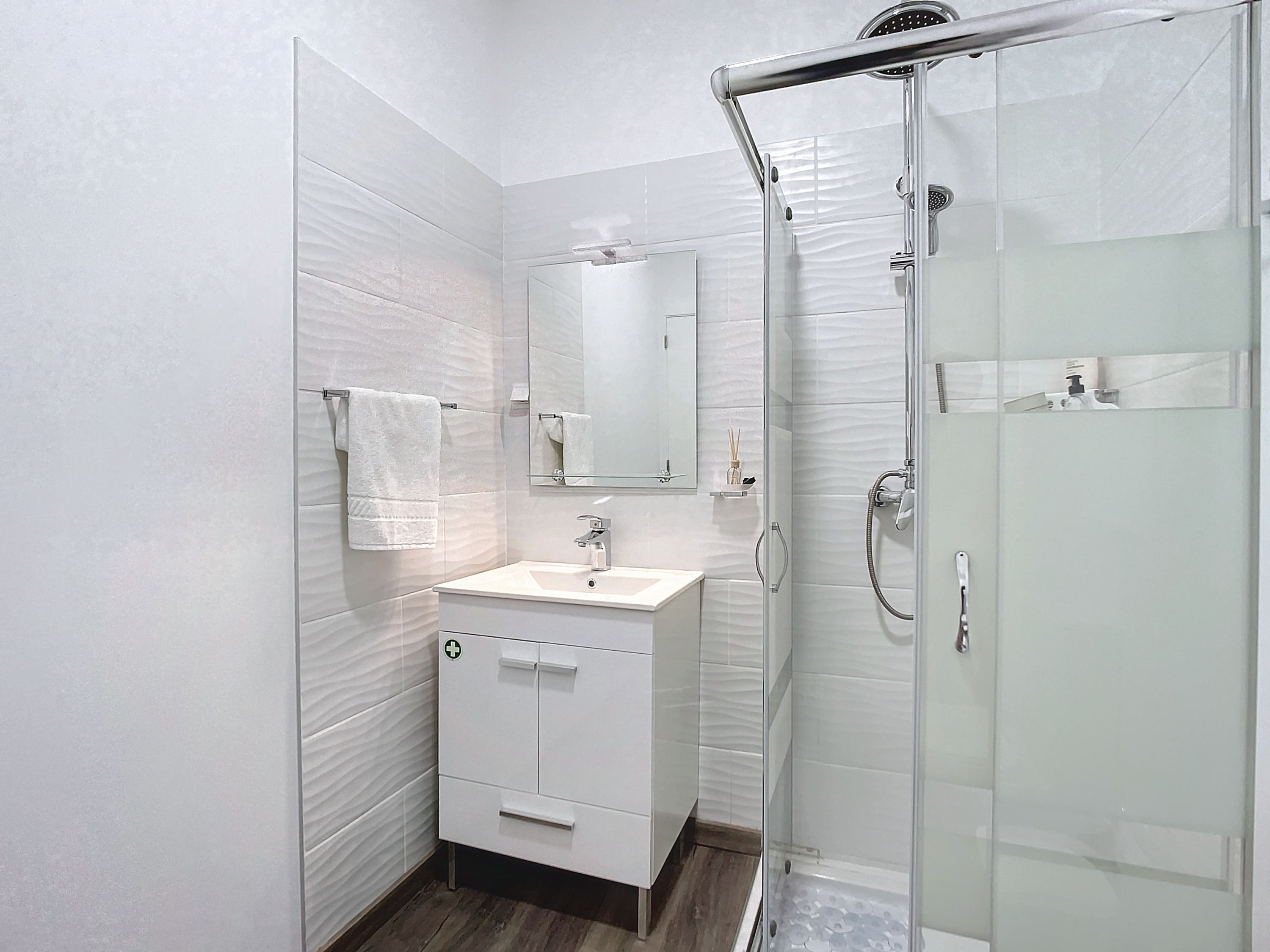 Une salle de bain moderne avec une douche à parois de verre, un meuble-lavabo blanc et un miroir au-dessus du meuble-lavabo.