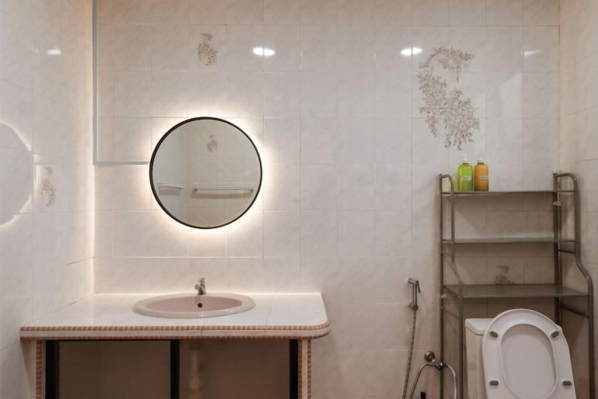 A bathroom with a round mirror, a sink, a toilet, and a shelf with toiletries.