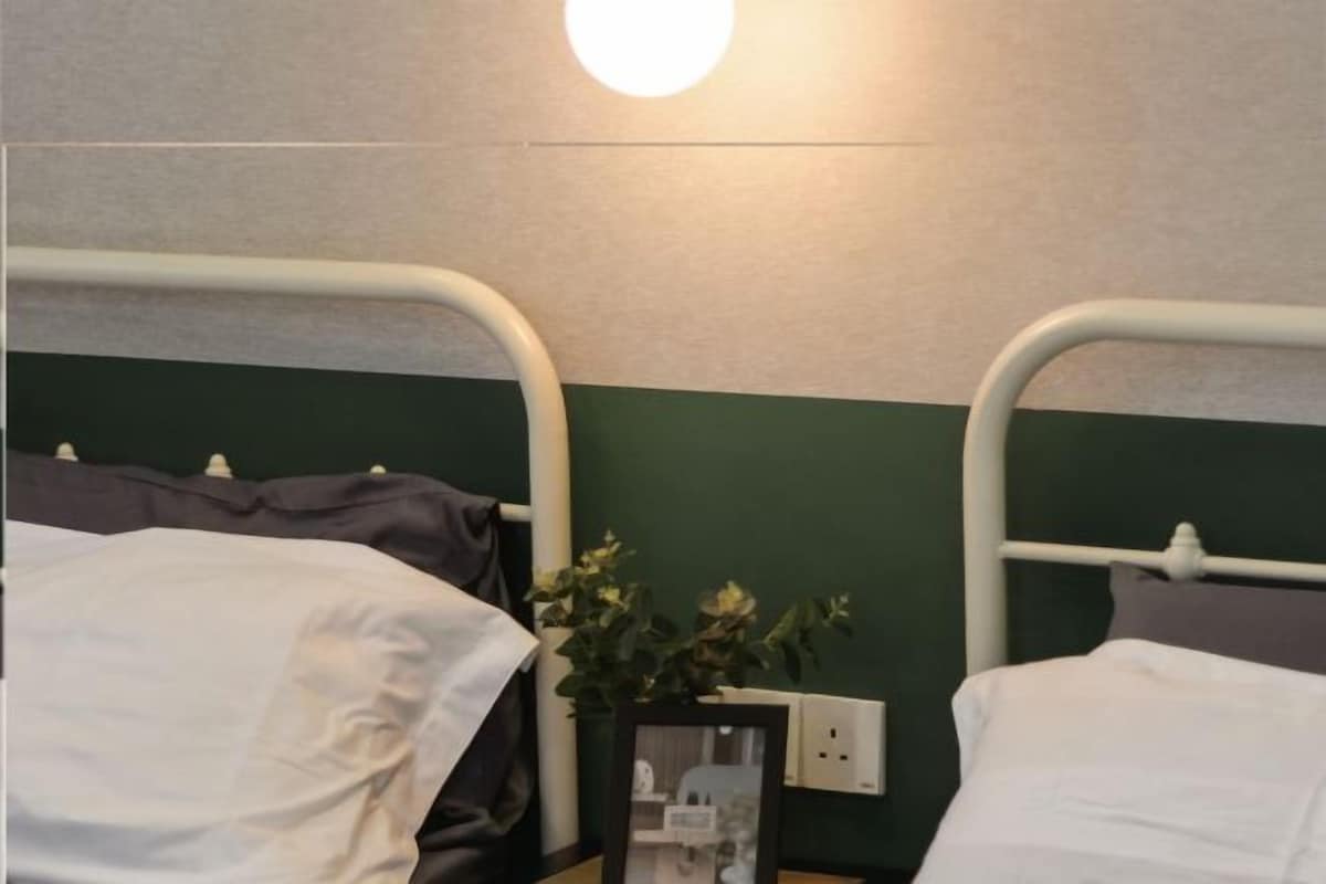 A twin room with two beds, a bedside table, a wall-mounted light, and a power outlet.