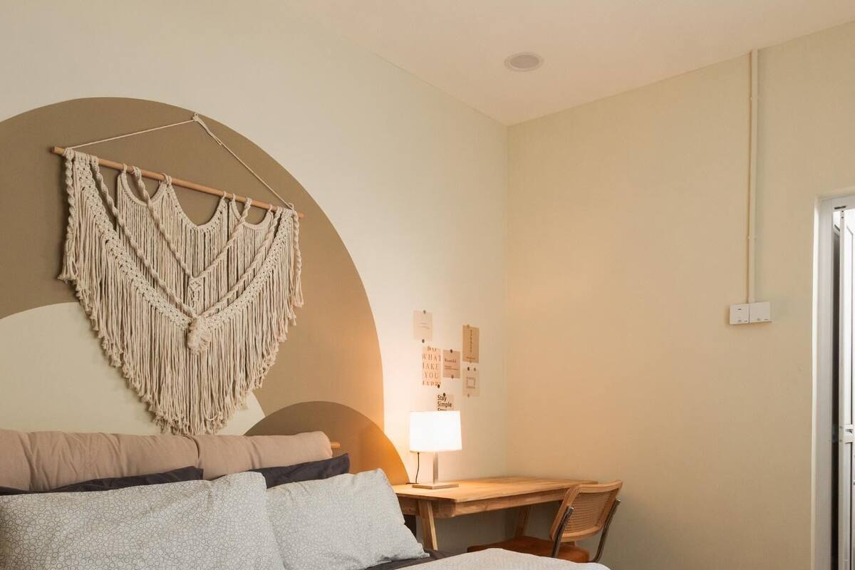 A bedroom with a bed, a desk, and a macrame wall hanging.