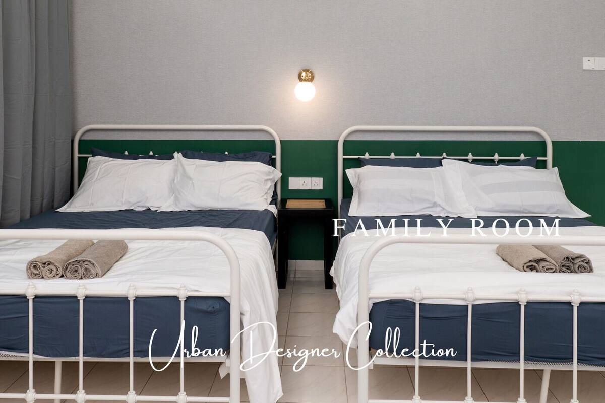 A family room with two beds, each with white bedding and green headboards. There is a wall-mounted light fixture above the beds.