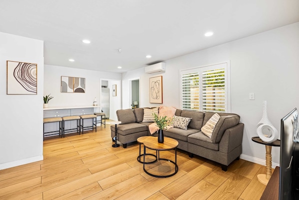 Una sala moderna con un sofá gris, una mesa de centro de madera y un mueble para televisión con un objeto decorativo.