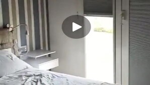 Une chambre à coucher comprenant un lit, une table de chevet, une lampe, une fenêtre avec des stores et une porte.