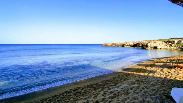Une plage à l’eau d’un bleu limpide, bordée d’une étendue de sable et de falaises rocheuses.