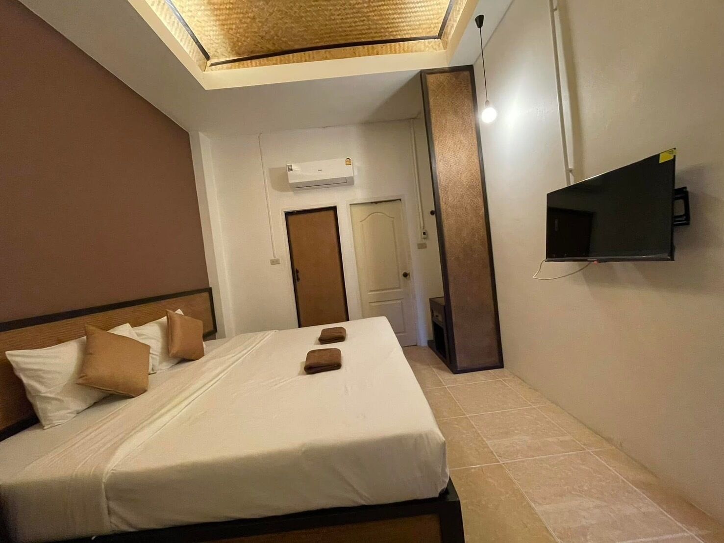 A hotel room with a bed, a flat-screen TV mounted on the wall, and an air conditioning unit on the wall.