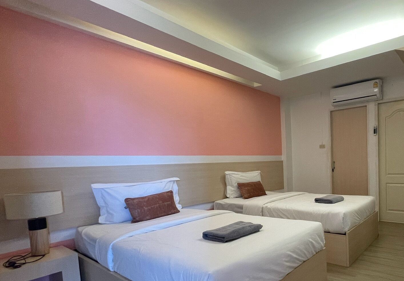 A hotel room with two beds, a nightstand, a lamp, and an air conditioning unit.