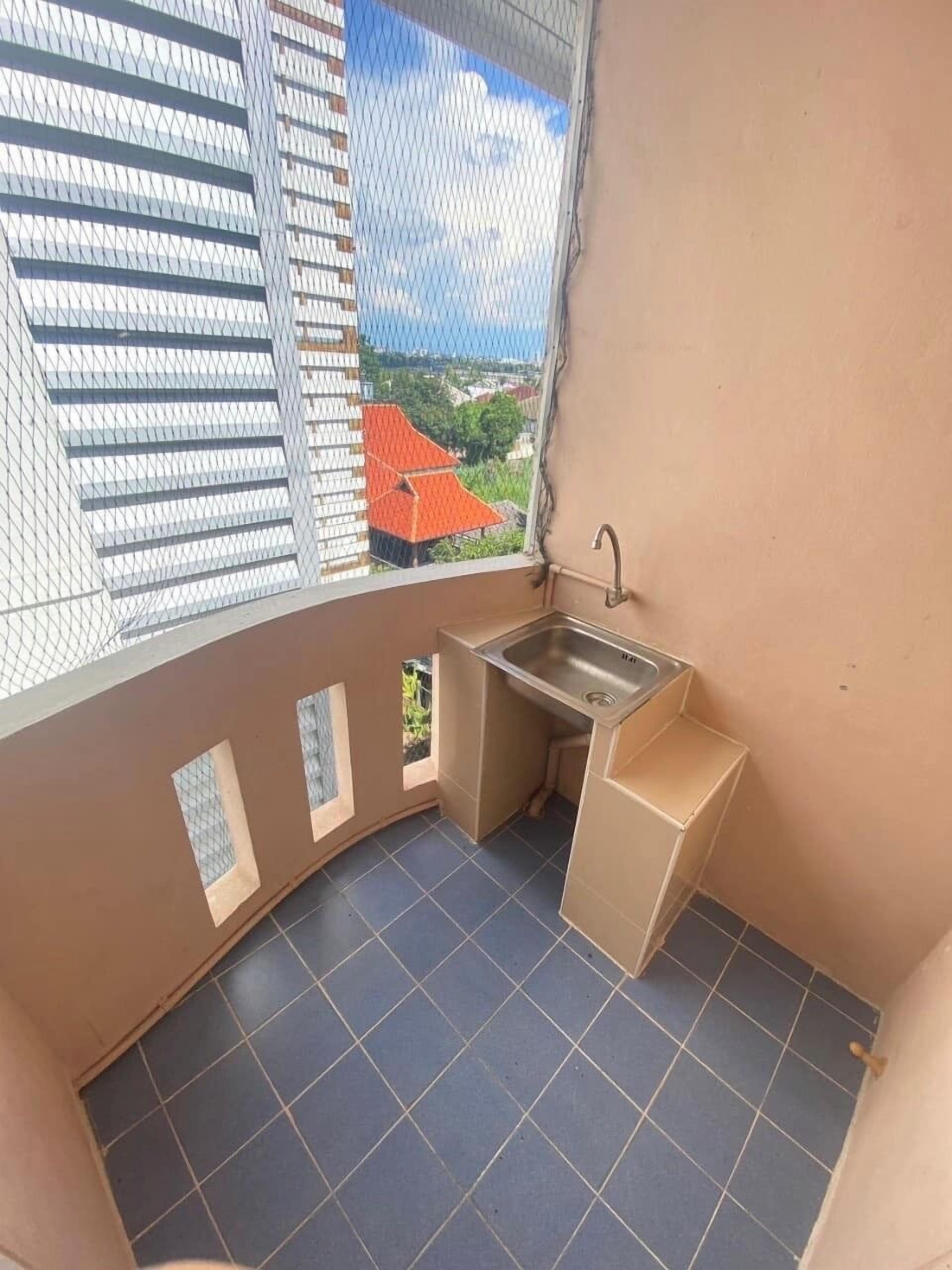 A small balcony with a sink, tiled floor, and a view of a red-roofed building.