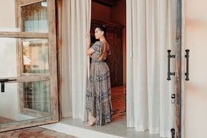 A person standing at a doorway with a patterned dress, wooden door frame, and a glass window.