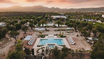 A resort with a central pool, multiple lounge areas, and a mountainous backdrop.