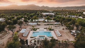 Un resort con piscina central, varias zonas de descanso y montañas al fondo.