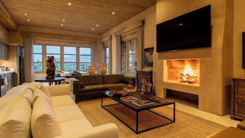 A spacious living room with a fireplace, a sofa, a coffee table, and a television mounted on the wall.
