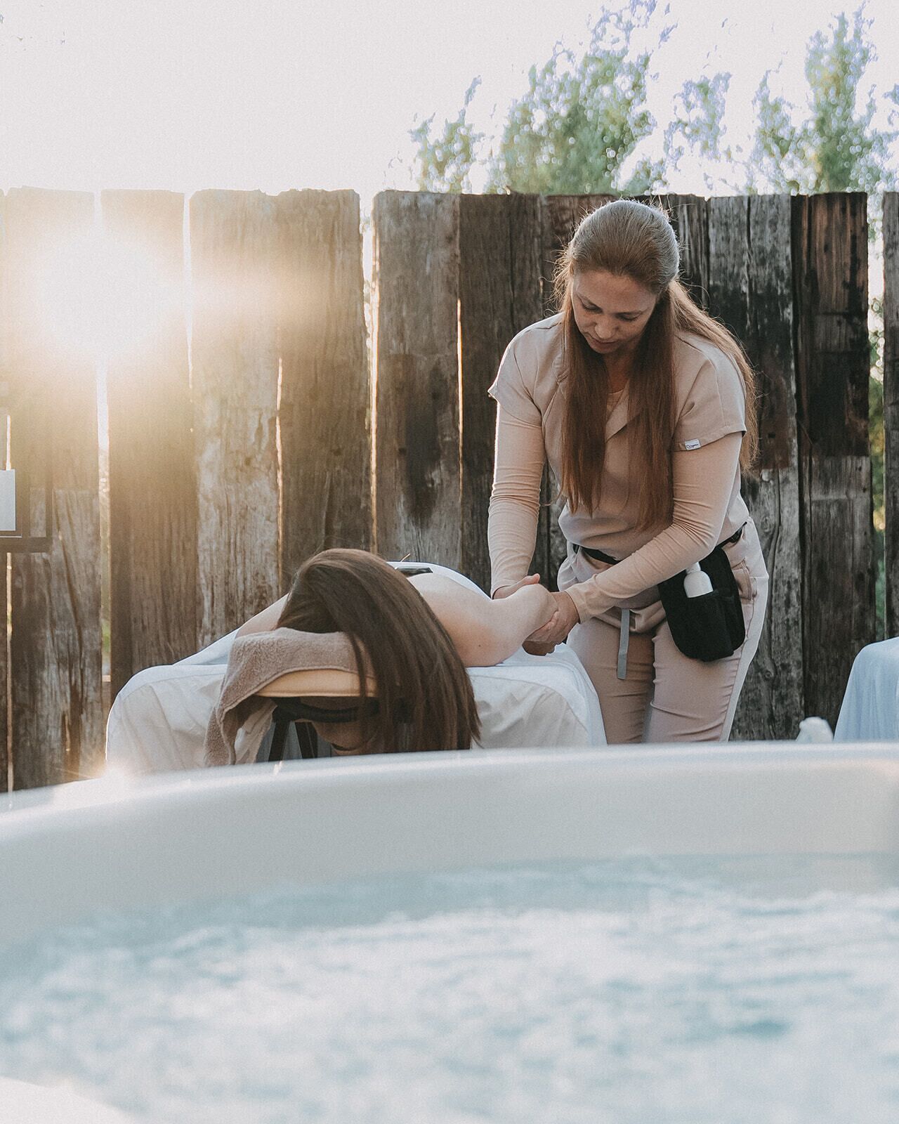 A person lying in a hot tub with another person attending to them.