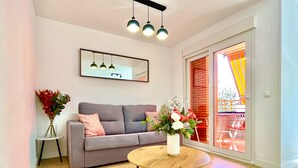 Un salon moderne avec un canapé gris, une table basse ronde en bois, un vase blanc orné de fleurs et un grand miroir accroché au mur.