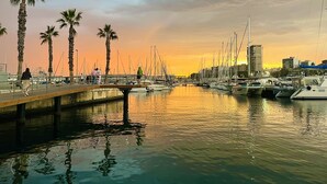 Un port de plaisance avec des bateaux amarrés, des palmiers et un coucher de soleil en arrière-plan.