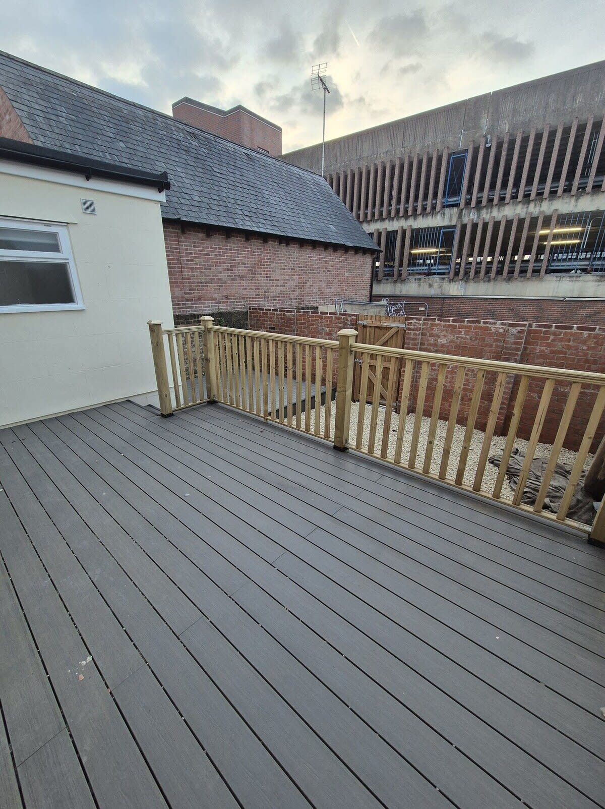 A wooden deck with a metal railing, a brick building, and a clear sky.