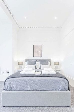 Een moderne slaapkamer met een groot bed, twee nachtkastjes en een ingelijste afbeelding aan de muur.
