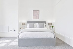 A modern bedroom with a large bed, bedside tables, and a wall-mounted artwork.
