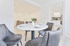 A modern dining area with a round table set for four, surrounded by grey upholstered chairs. - Spacious 1 Bed Apartment in Cheltenham w Terrace (Cheltenham)