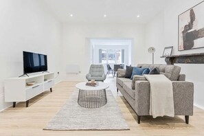 A modern living room with a flat-screen TV, a grey sofa, a coffee table, and a white entertainment unit.