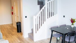Un salon moderne comprenant un canapé, une table basse ronde avec une plante, une table à manger avec des chaises et un escalier.