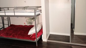 Ein Etagenbett mit roter Decke und Kissen, eine weiße Wand mit Schmetterlingsmotiven und eine Tür, die zu einem Flur führt.