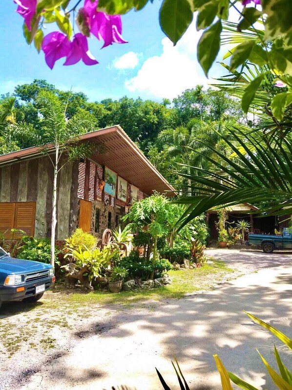 A rustic building with a corrugated metal roof, surrounded by lush greenery and a parked car. - Baan Pak Rim Kuaen Resort (Ban Ta Khun)