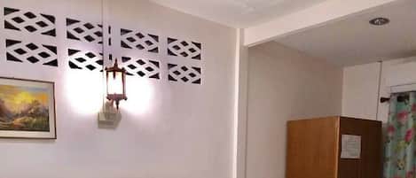 Habitación de hotel con cama, armario de madera, mesita de noche, lámpara de pared y un cuadro.