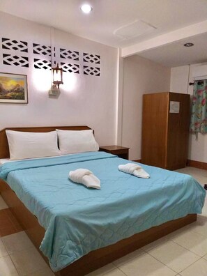 A hotel room with a bed, a wooden wardrobe, a nightstand, a wall-mounted light fixture, and a painting. - Baan Pak Rim Kuaen Resort (Ban Ta Khun)