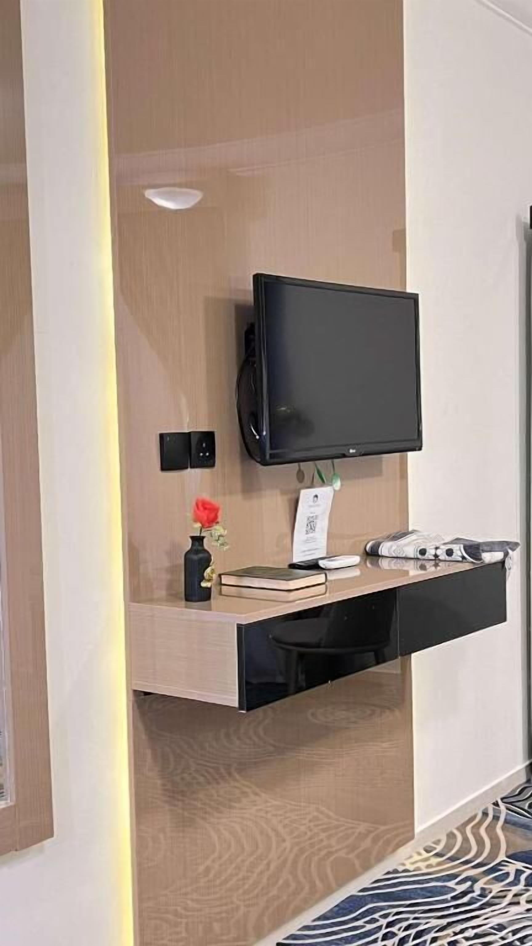 A modern hotel room with a built-in desk, a flat-screen TV, a vase with flowers, and a small plant.