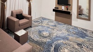Una moderna camera d'hotel con un letto grande, un'area relax con una poltrona, una televisione a schermo piatto e un ampio specchio.