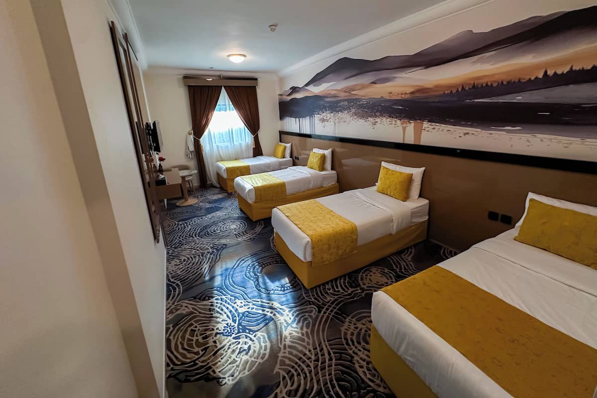 A hotel room with three beds, a large mural, and a patterned carpet.