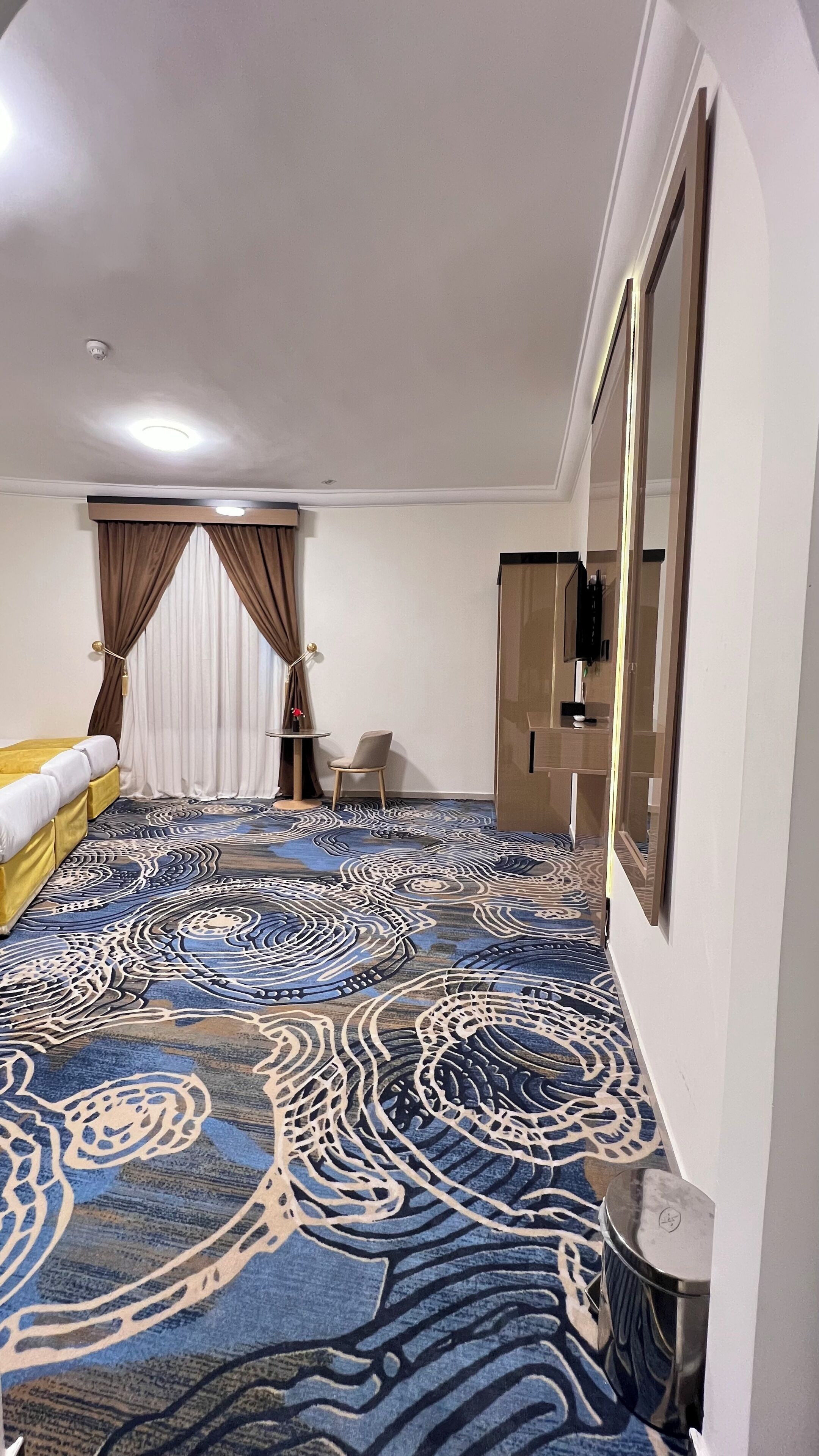 A hotel room with a patterned carpet, a bed, a chair, a TV, and a wardrobe.