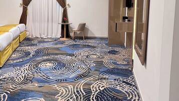 A hotel room with a patterned carpet, a bed, a chair, a TV, and a wardrobe.