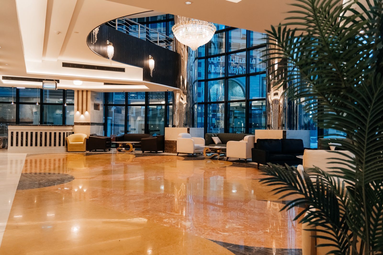 A modern lobby with a curved staircase, large windows, and a chandelier.