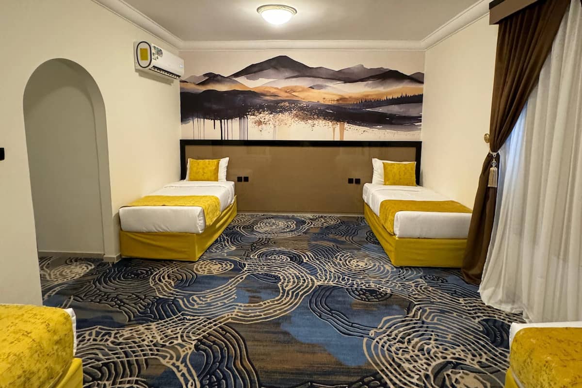 A hotel room with two beds, a mural of a mountain landscape, and a patterned carpet.