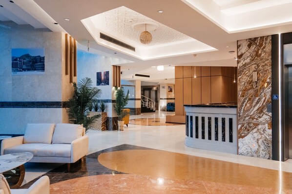 A modern lobby with a reception desk, seating area, and a staircase leading to upper floors. - Capital Guest hotel فندق كابيتال جيست العزيزية الجنوبية (Makkah)