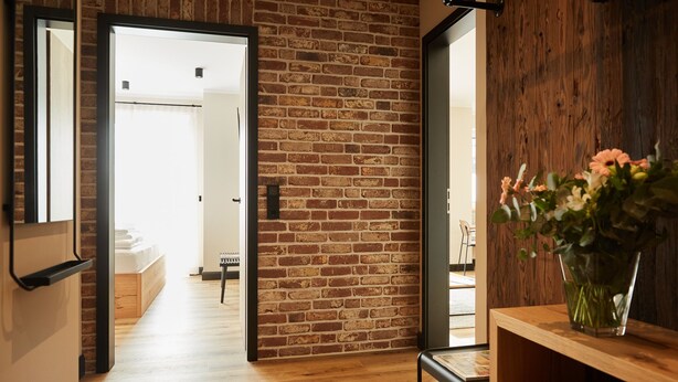 A modern interior with a brick wall, wooden flooring, and a wooden shelf with a vase of flowers. - Binnendiek Resort Büsum Haus 6 - Apartment 6 (Büsum)