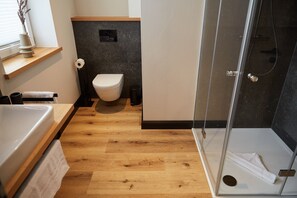 A modern bathroom with a toilet, shower, and wooden flooring. - Binnendiek Resort Büsum Haus 6 Comfort - Apartment 7 (Büsum)