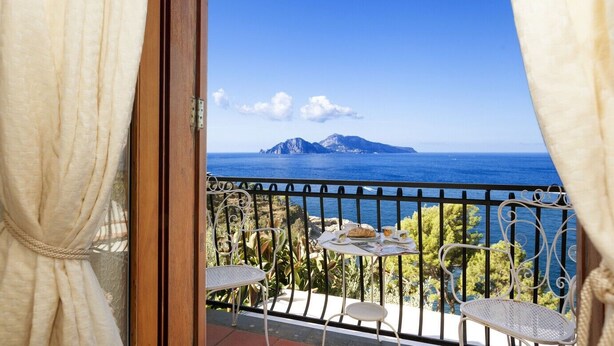 Un balcón con una mesa para dos, con vistas a la costa y una montaña al fondo.