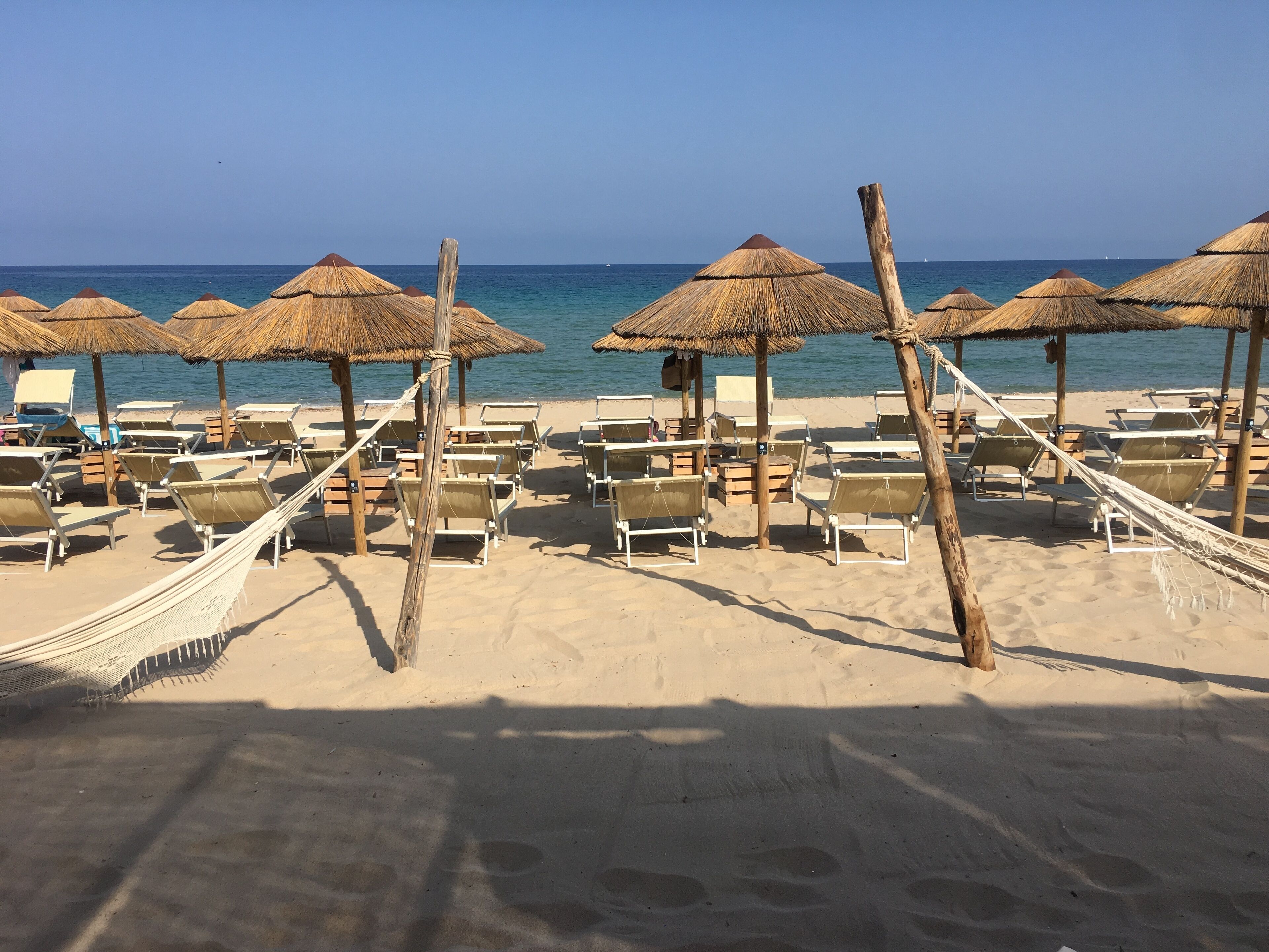 A beach with thatched umbrellas and sun loungers arranged in rows.