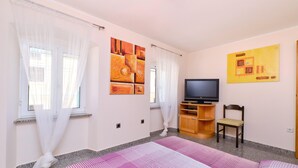 Quarto com cama, televisão, uma cadeira e obras de arte nas paredes.