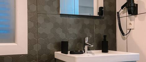 A bathroom with a white sink, a mirror, and a hairdryer mounted on the wall.