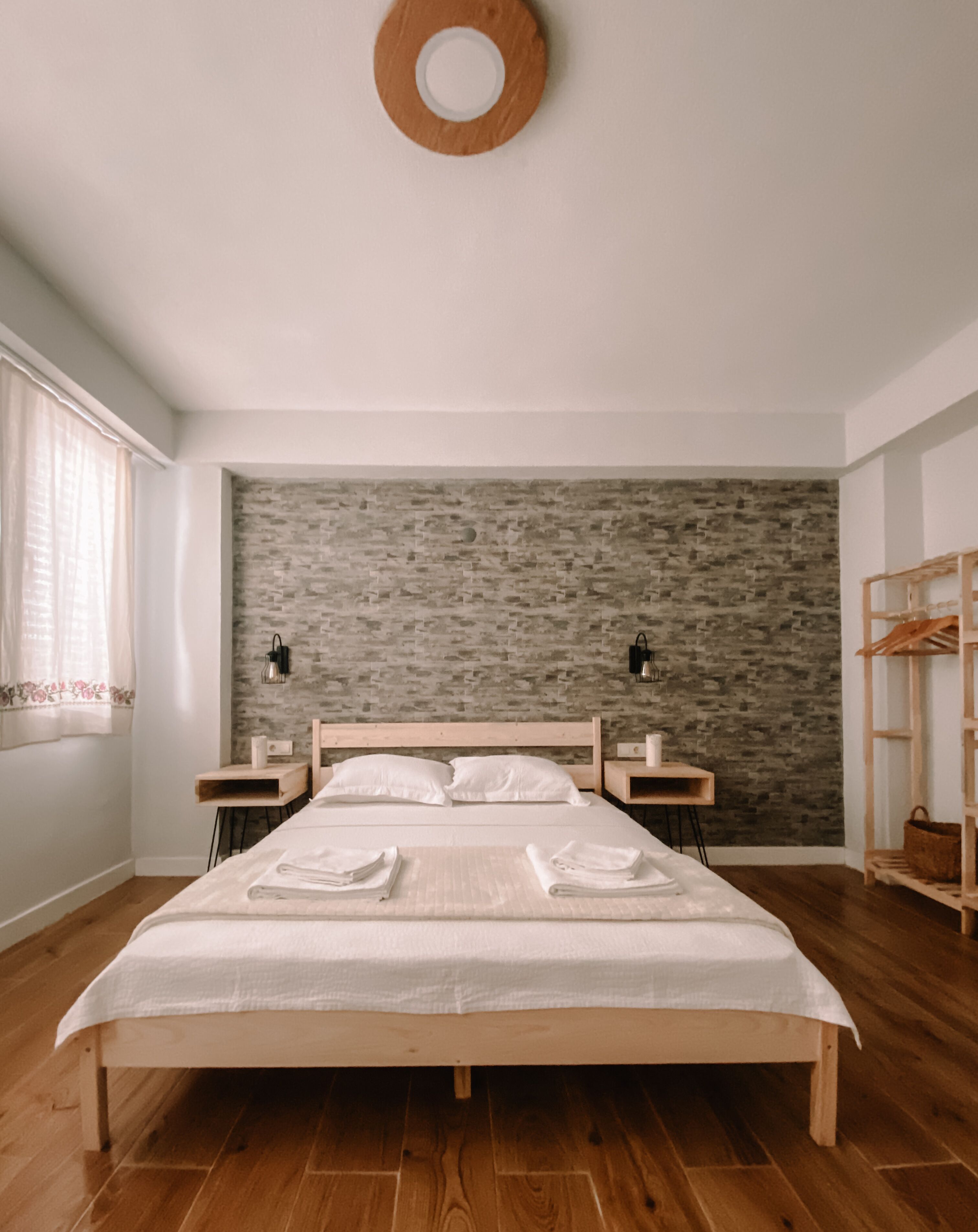 Ein ordentlich bezogenes Bett mit weißen Leinen, einem hölzernen Kopfteil und einer Wand im Backsteinoptik dahinter.