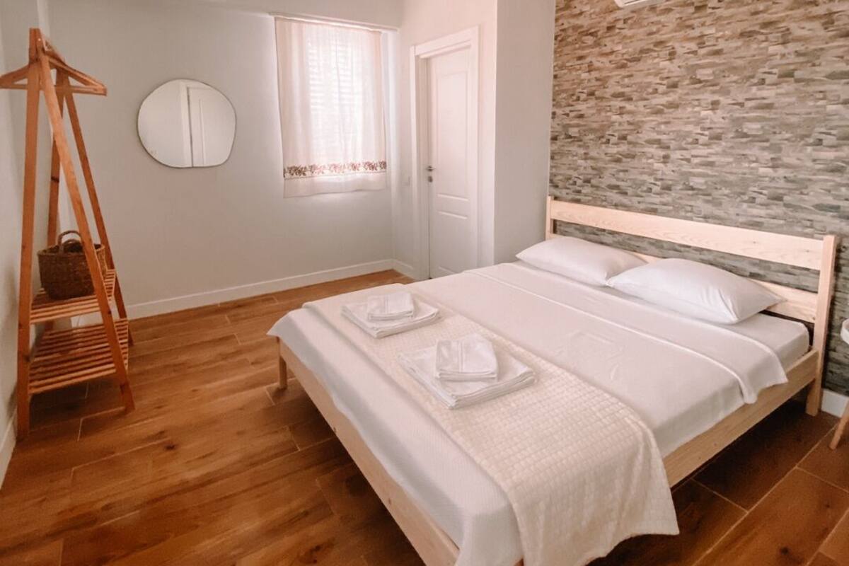 A bedroom with a wooden bed, a hanging chair, a round mirror, and a stone-patterned wall.