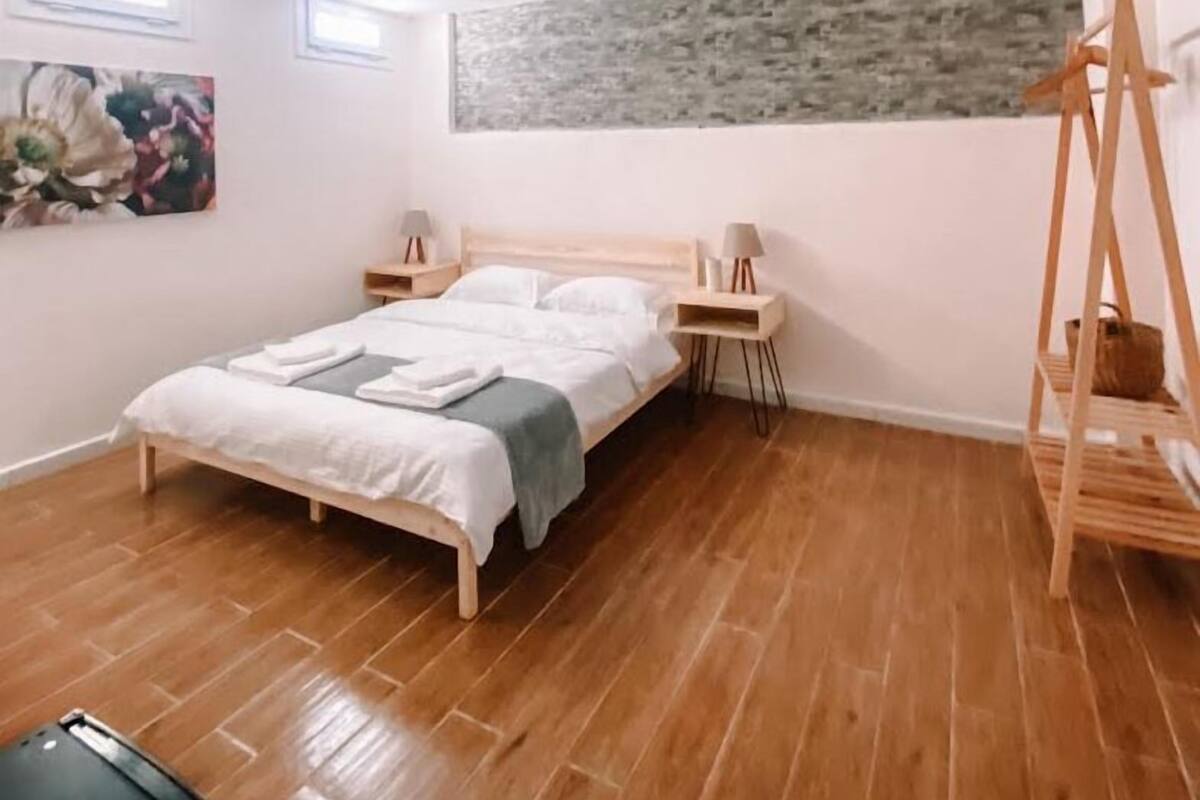 A bedroom with a wooden bed, two bedside tables, a wall-mounted shelf, and a painting.