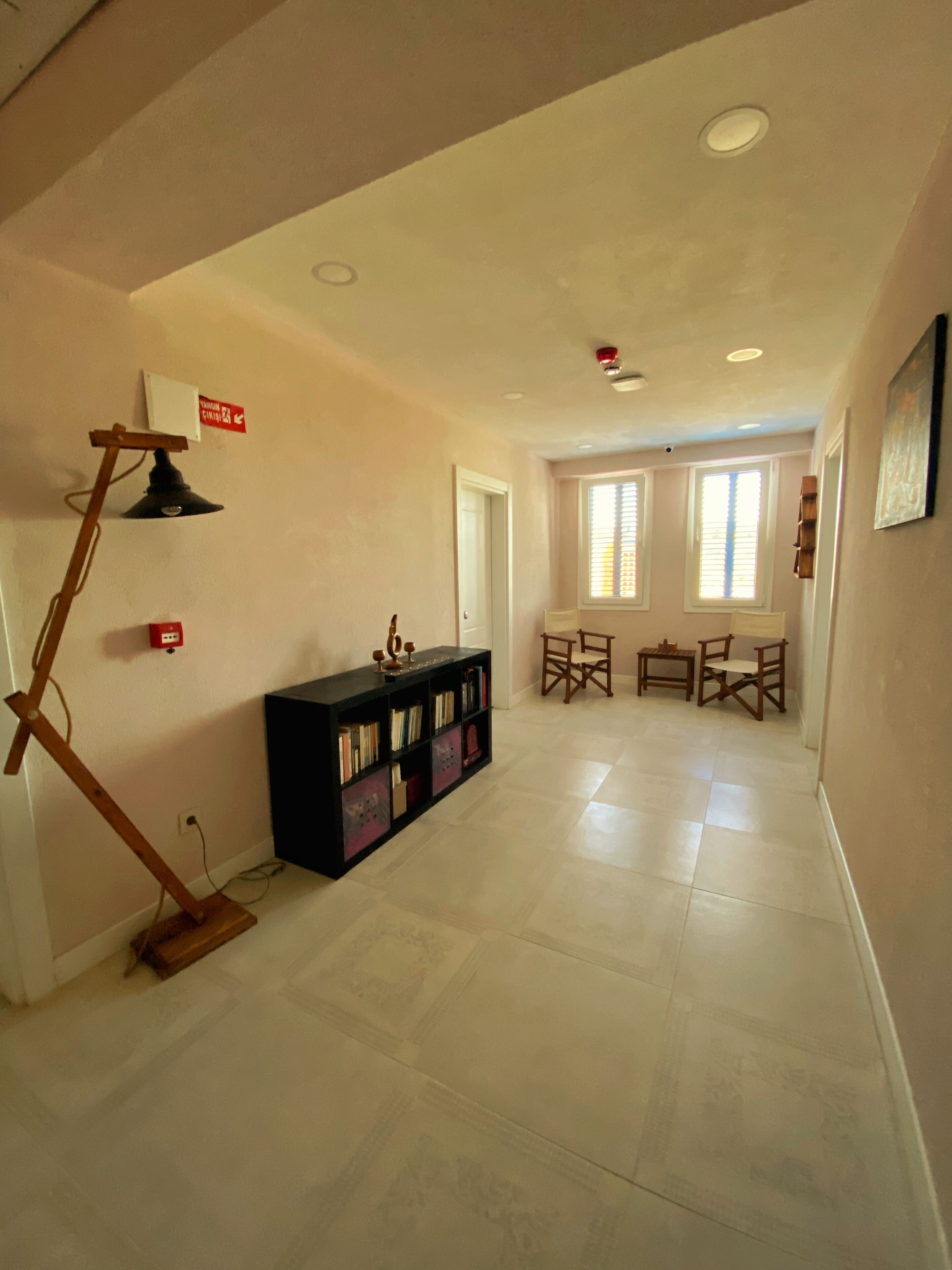 A spacious room with a black bookshelf, a wooden floor lamp, and a dining area with two chairs and a table.