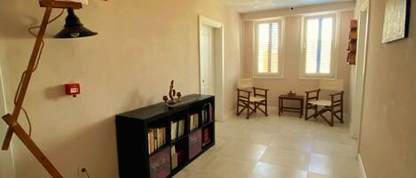 A spacious room with a black bookshelf, a wooden floor lamp, and a dining area with two chairs and a table.