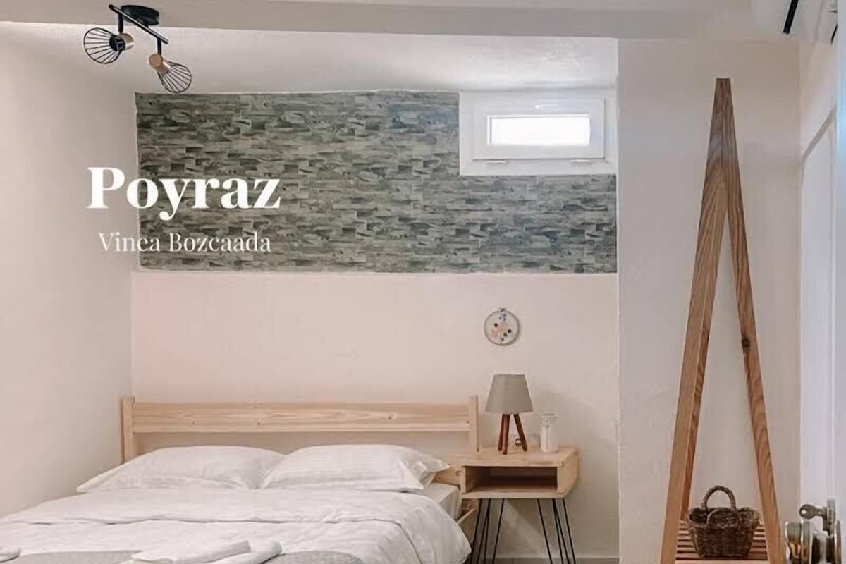 A bedroom with a wooden bed, a bedside table with a lamp, a small window, and a wooden ladder against the wall.