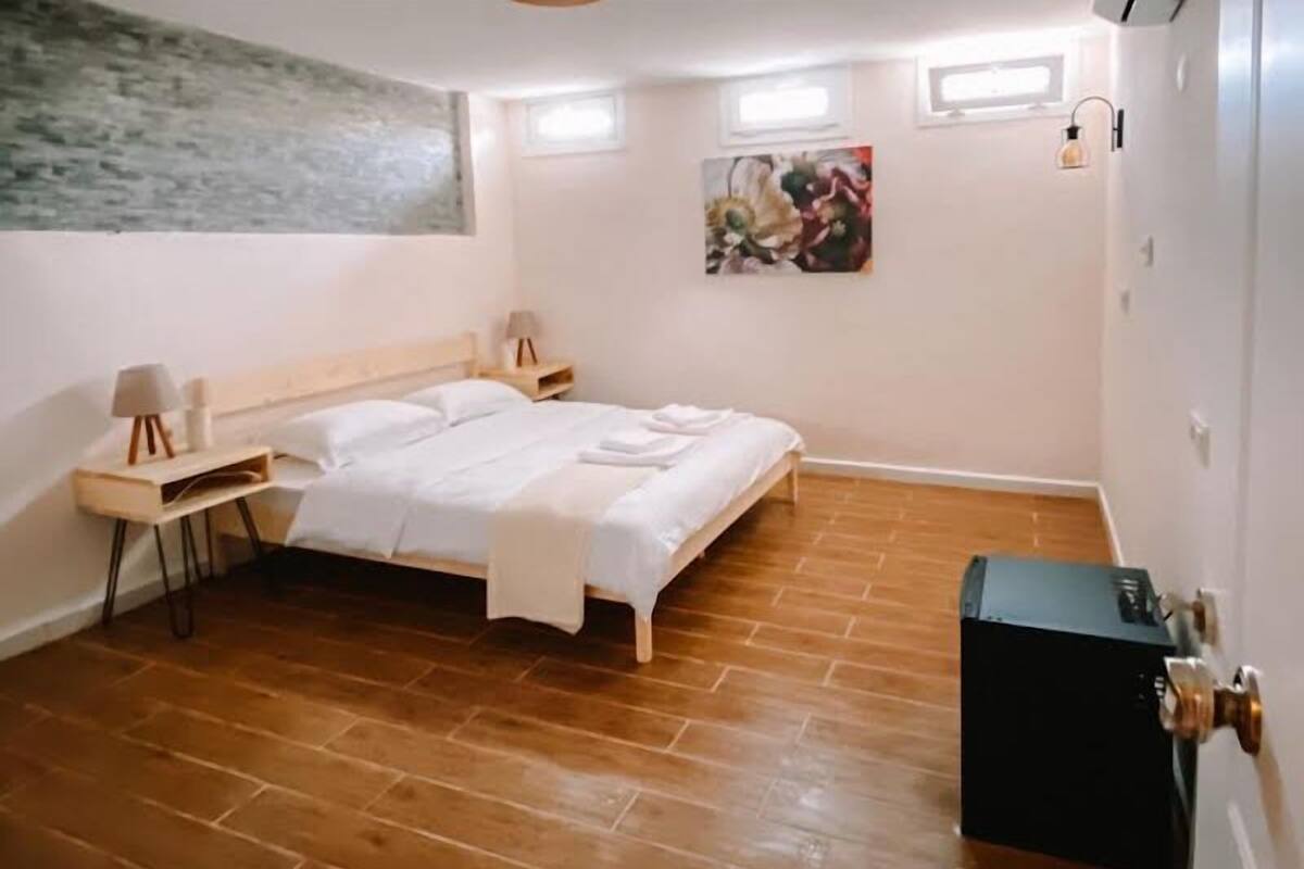 A bedroom with a wooden floor, a bed with white bedding, a bedside table with a lamp, and a painting on the wall.