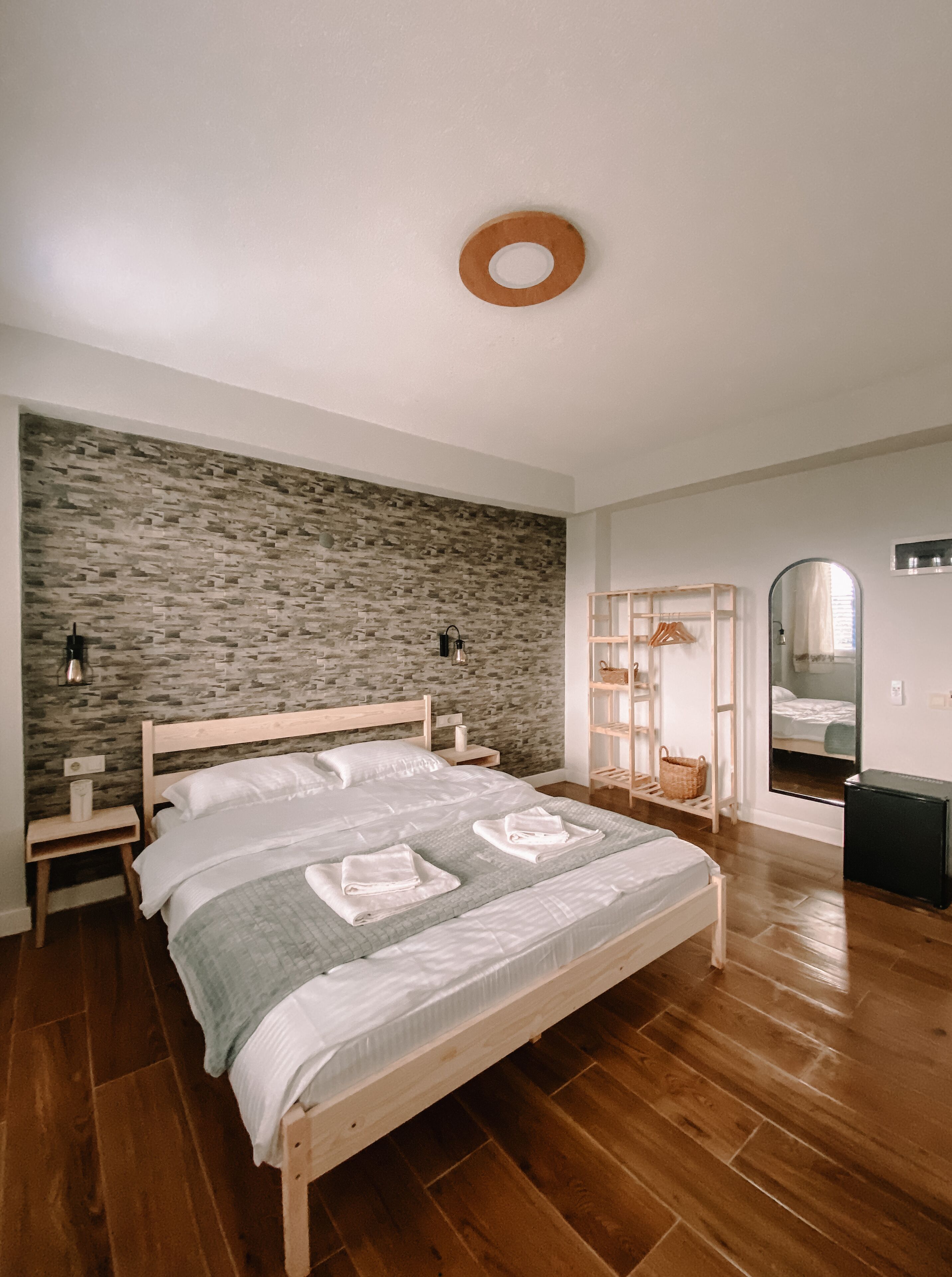 A bedroom with a stone wall, wooden bed, bedside tables, a mirror, and a wardrobe.